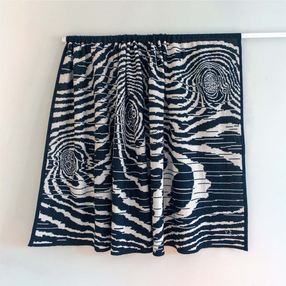 The folded wool drapery seen complete, mounted on a curtain track on the wall, 
showing the substance, pattern, context