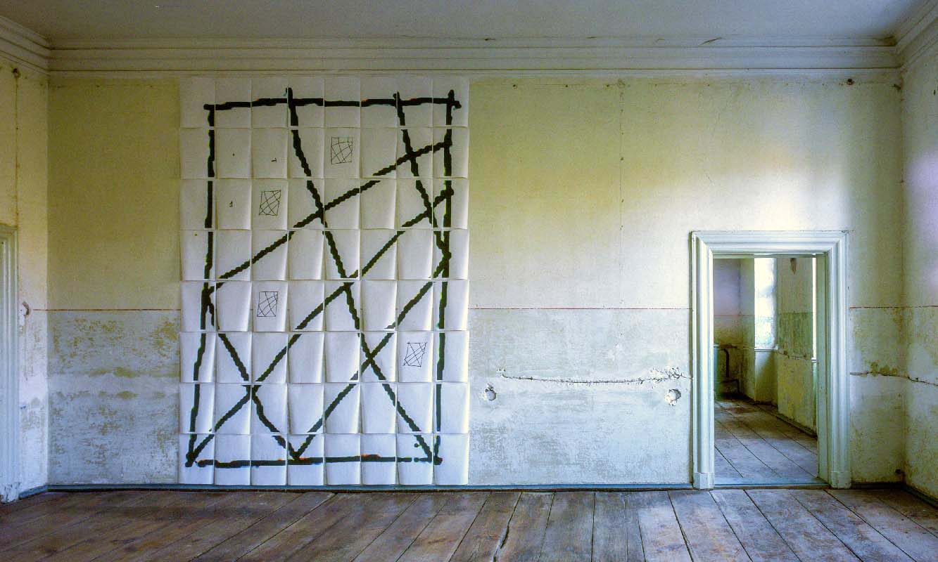 In one large empty room, a geometric grid drawing fill the wall, daylight coming in 
from an unseen window right